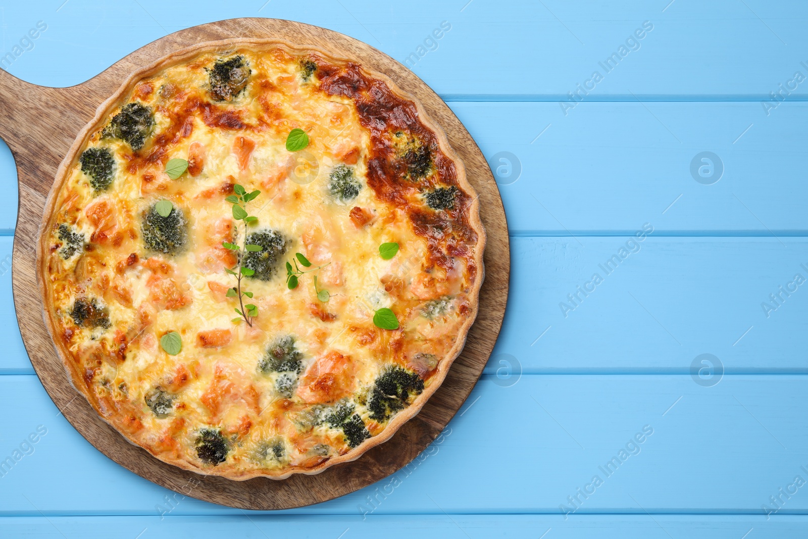 Photo of Delicious homemade quiche with salmon and broccoli on light blue wooden table, top view. Space for text
