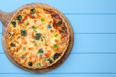 Delicious homemade quiche with salmon and broccoli on light blue wooden table, top view. Space for text