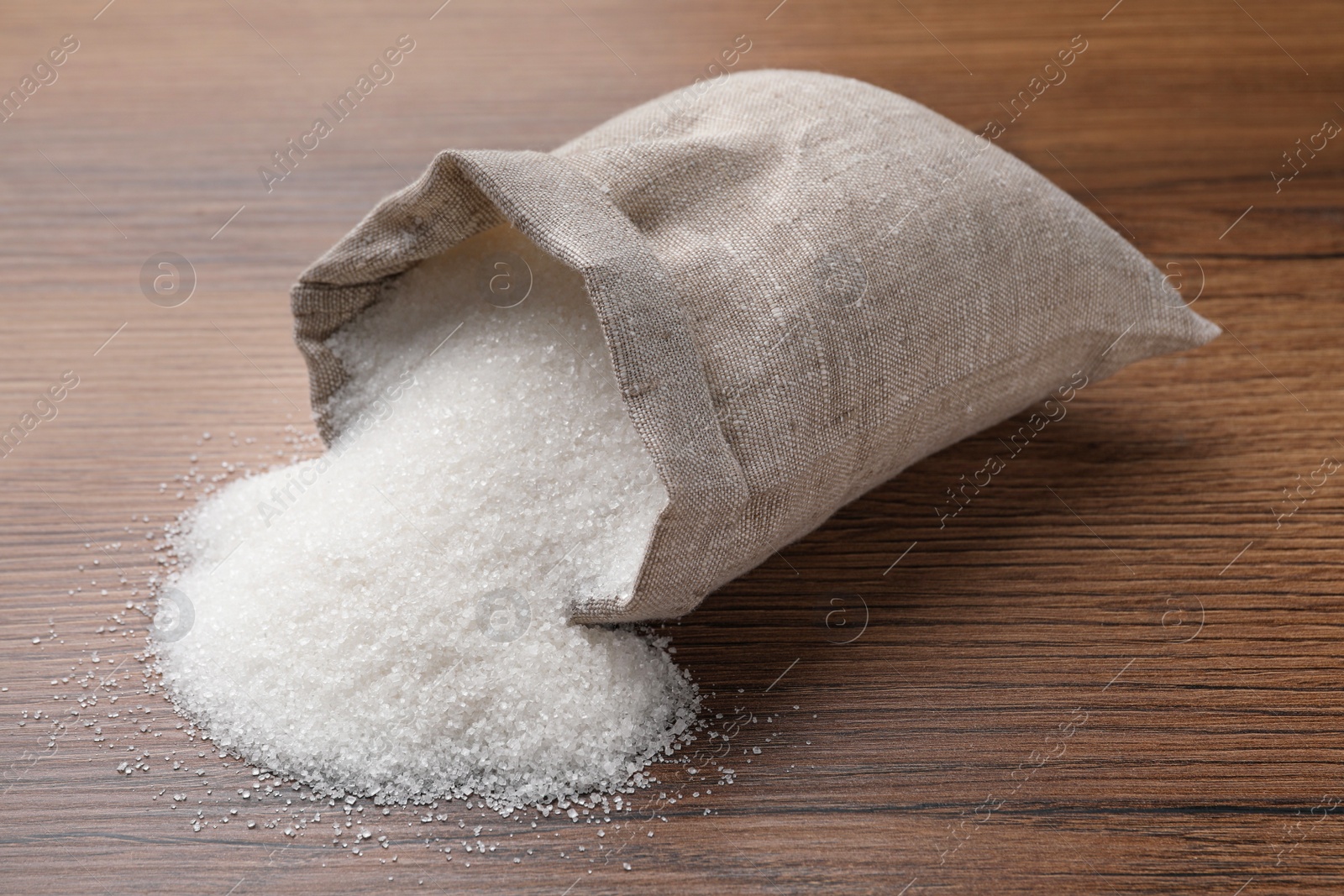 Photo of Overturned sack bag with granulated sugar on wooden table