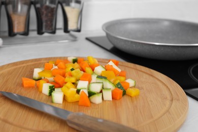 Photo of Wooden board with cut vegetables and knife near frying pan in kitchen, closeup
