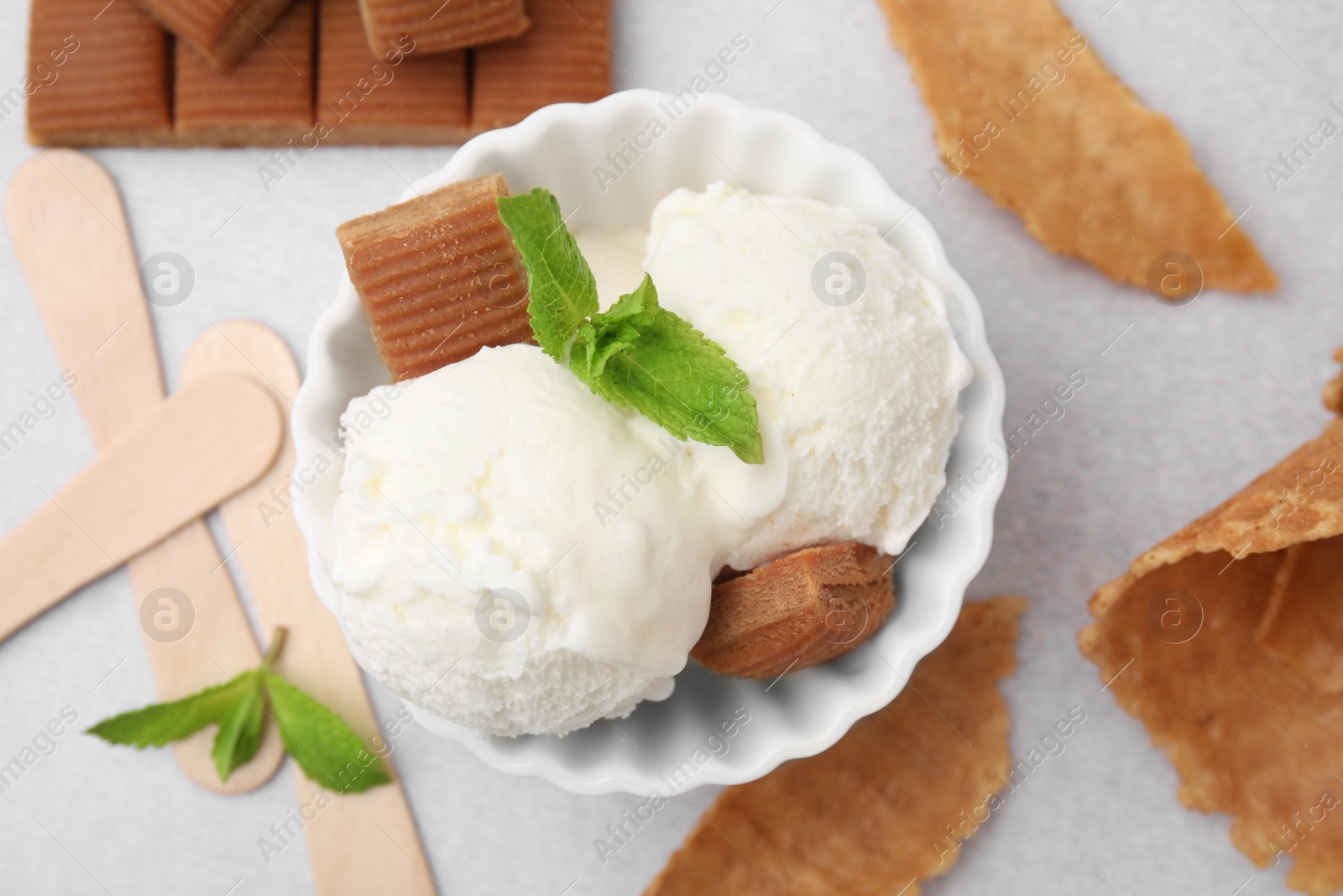 Photo of Scoops of tasty ice cream with mint leaves and caramel candies on white table, flat lay