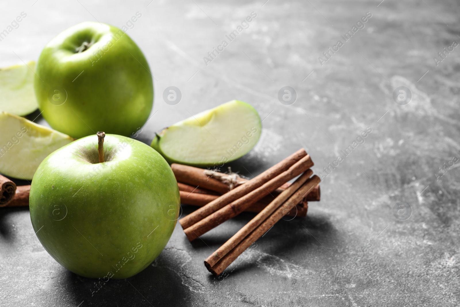 Photo of Fresh apples and cinnamon sticks on gray table