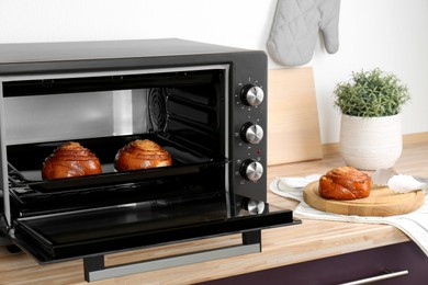 Photo of Open electric oven with delicious pastry on wooden table in kitchen