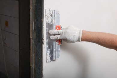 Worker plastering wall with putty knife indoors, closeup