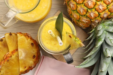 Tasty pineapple smoothie and fruit on wooden table, flat lay