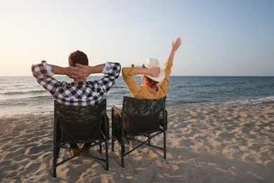 Couple sitting in camping chairs and enjoying seascape on beach, back view