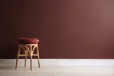 Photo of Stylish wooden stool with cushion near color wall, space for text. Interior element