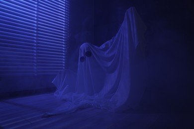 Photo of Creepy ghost. Woman covered with sheet near window in blue light