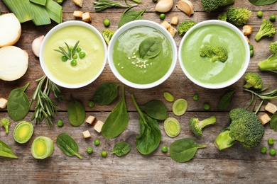 Flat lay composition with different fresh vegetable detox soups made of green peas, broccoli and spinach in dishes on wooden background