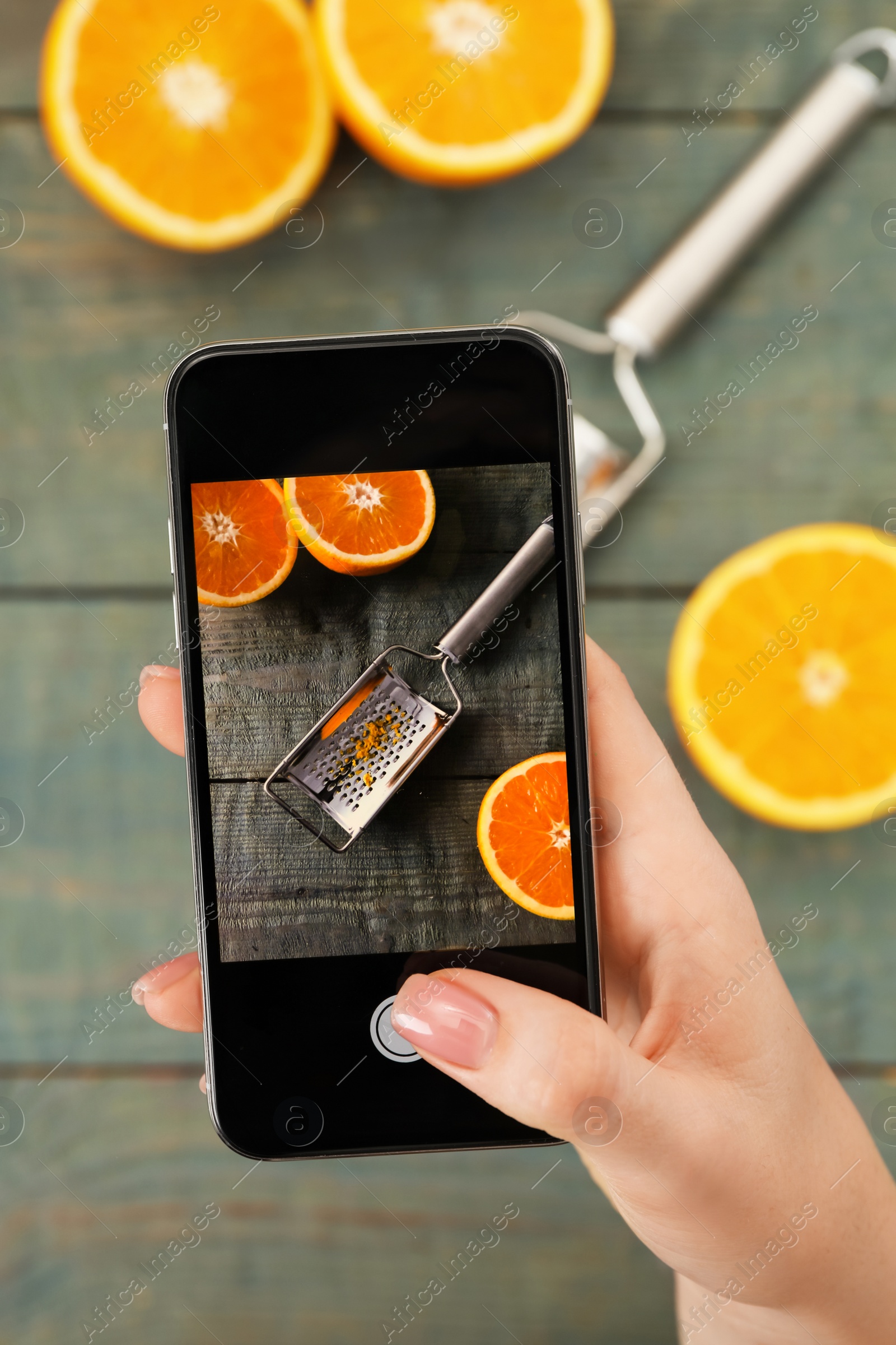 Photo of Woman taking picture of grater and oranges on wooden table, closeup