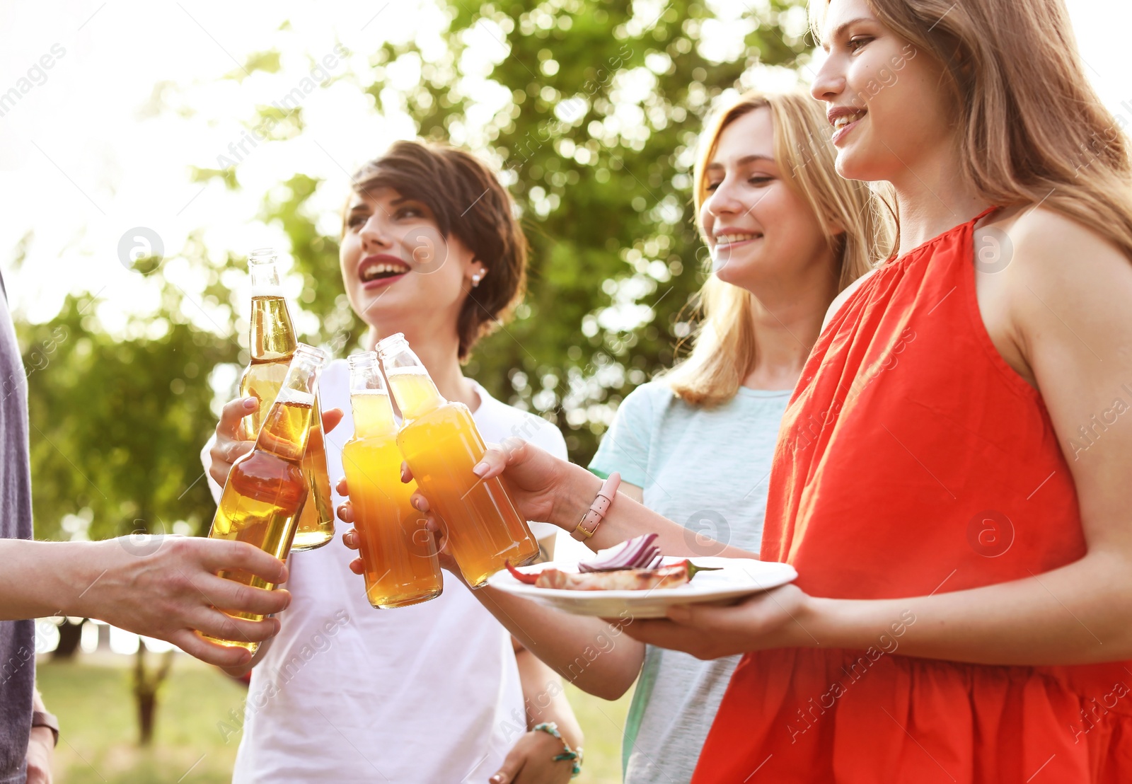 Photo of Young people with bottles of beer and food outdoors. Summer barbecue