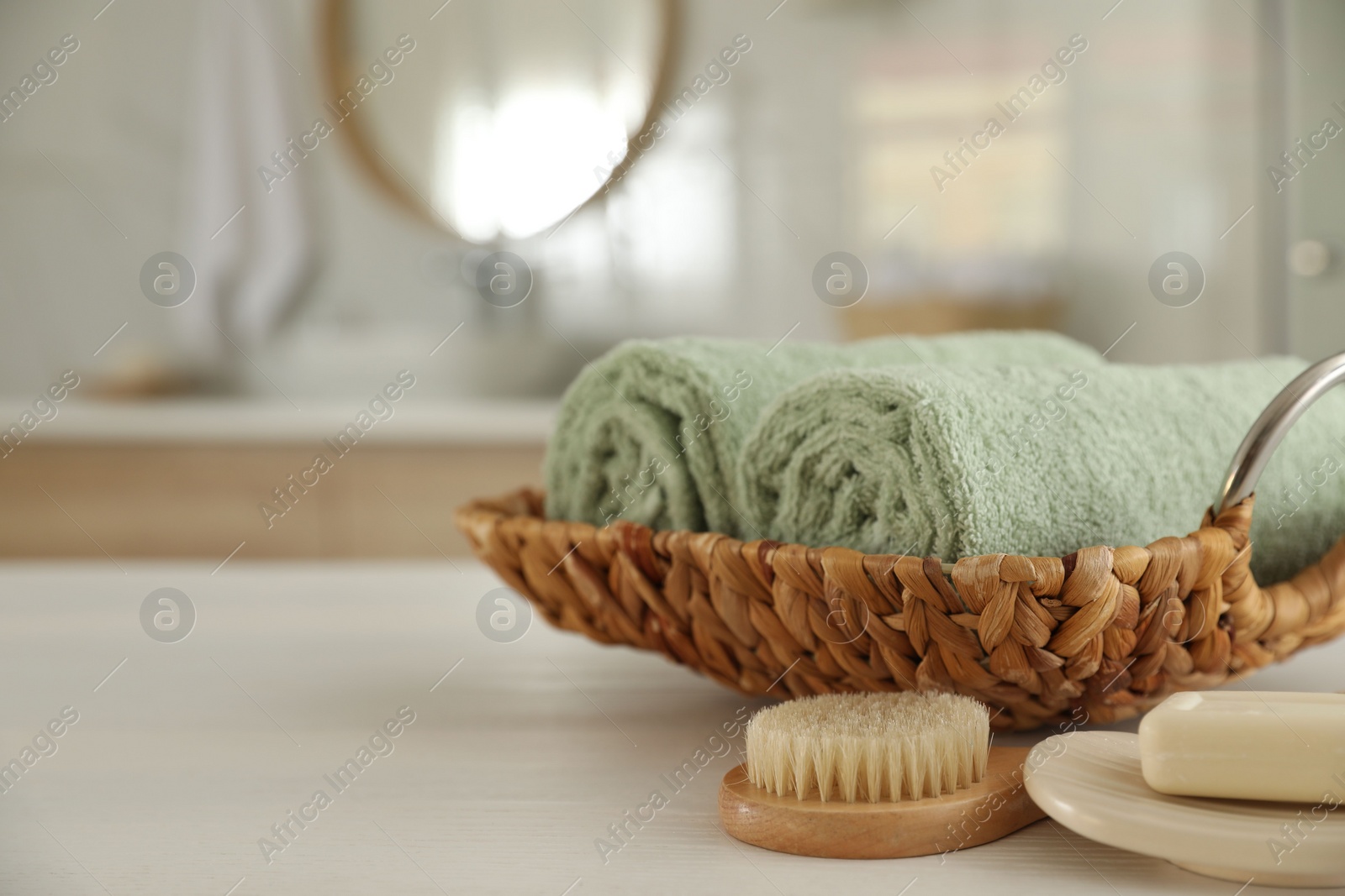 Photo of Wicker basket with rolled towels on white wooden table in bathroom. Space for text