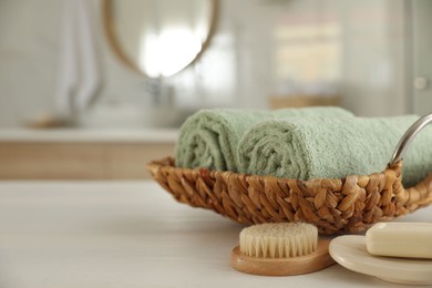 Wicker basket with rolled towels on white wooden table in bathroom. Space for text