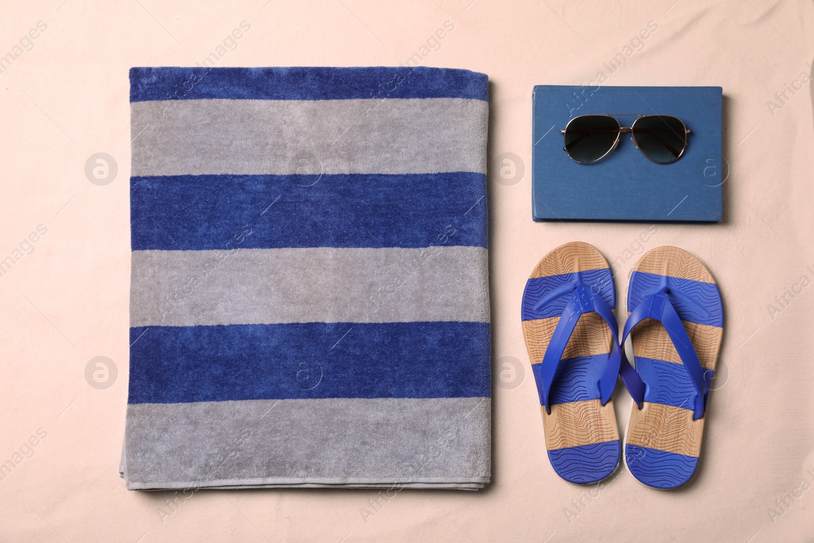 Photo of Beach towel, book, sunglasses and flip flops on sand, flat lay