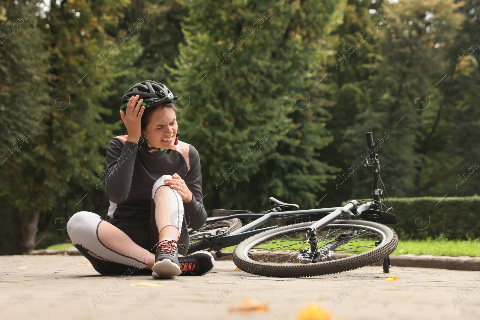 Photo of Young woman with injured knee near bicycle outdoors