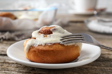 Photo of Tasty cinnamon roll with cream on wooden table, closeup