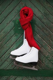 Pair of ice skates with knitted scarf hanging on green wooden wall