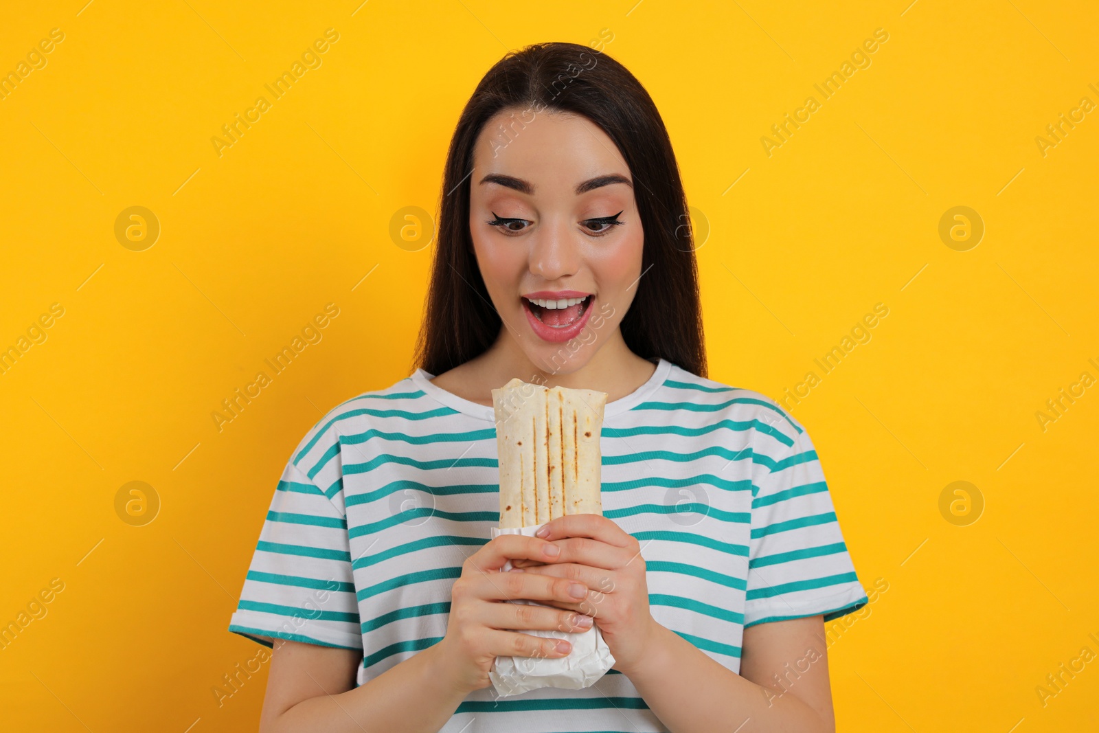 Photo of Young woman eating tasty shawarma on yellow background