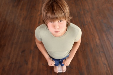 Photo of Emotional overweight boy standing on floor scales indoors, above view