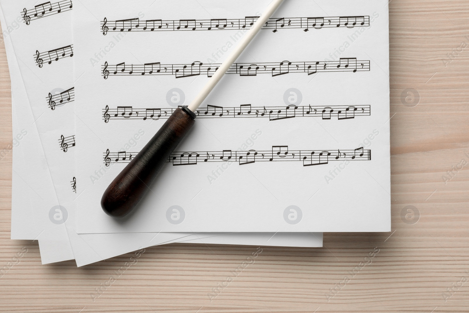 Photo of Conductor's baton and sheet music on white wooden table, top view