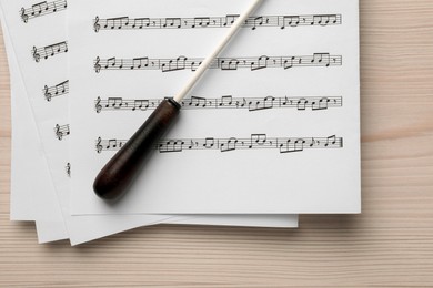 Photo of Conductor's baton and sheet music on white wooden table, top view