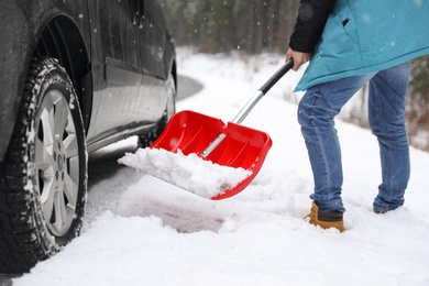 Photo of Man cleaning snow with shovel near stuck car outdoors