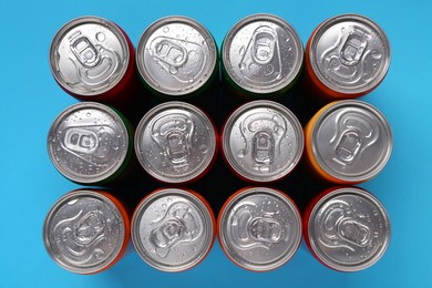 Energy drinks in wet cans on light blue background, top view