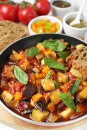 Photo of Dish with tasty ratatouille and basil on wooden board, closeup
