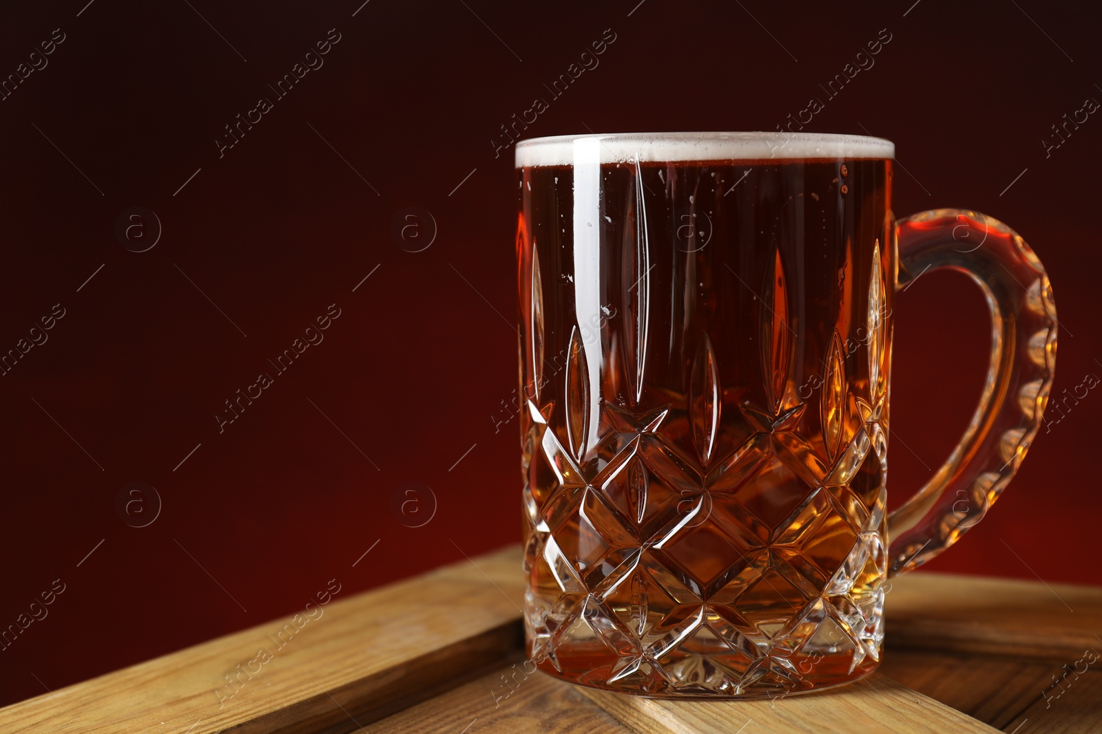 Photo of Mug with fresh beer on wooden crate against burgundy background, closeup. Space for text
