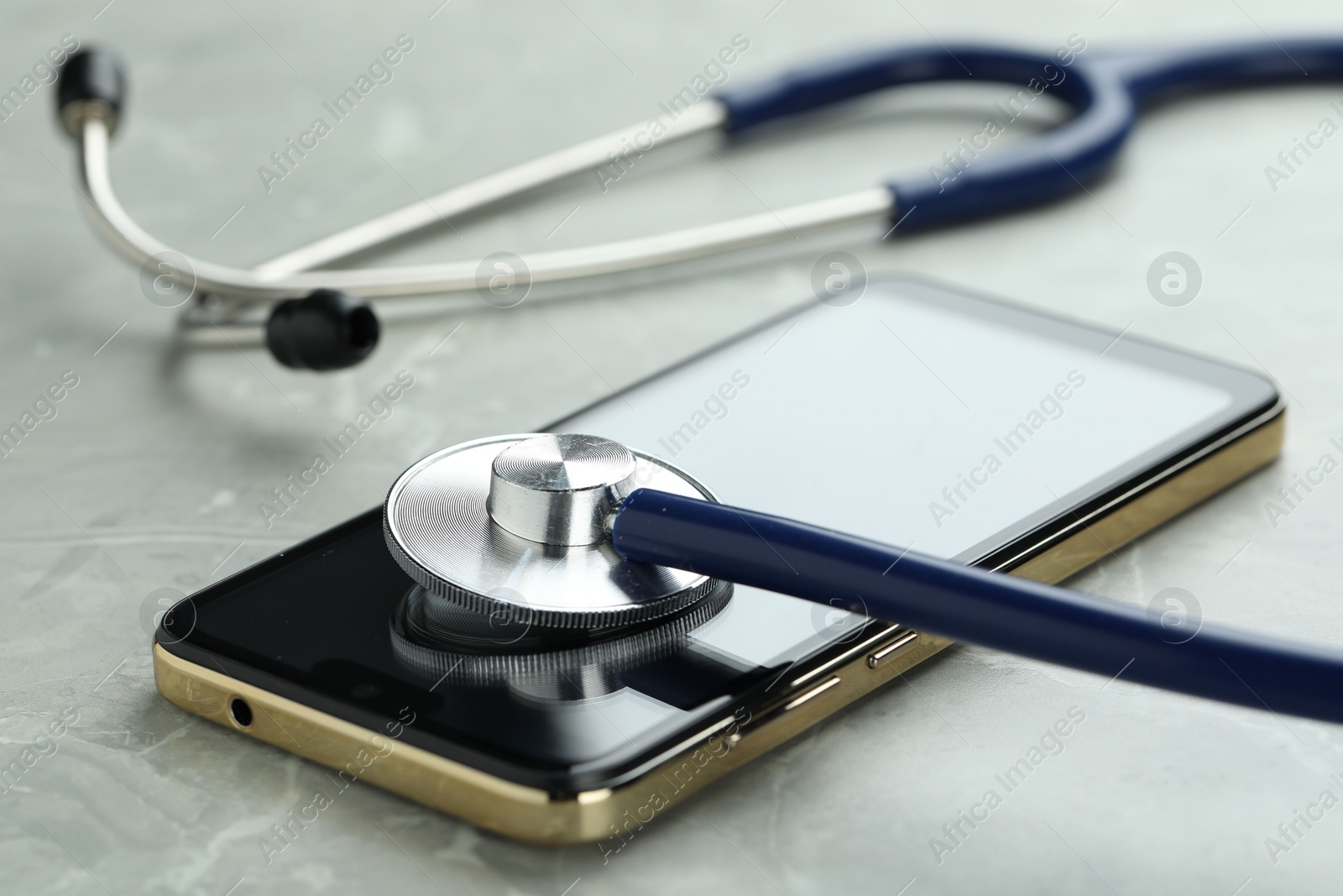 Photo of Modern smartphone and stethoscope on grey table, closeup