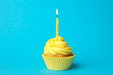 Delicious birthday cupcake with yellow cream and burning candle on light blue background