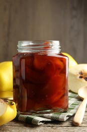 Photo of Tasty homemade quince jam in jar, spoon and fruits on wooden table, closeup