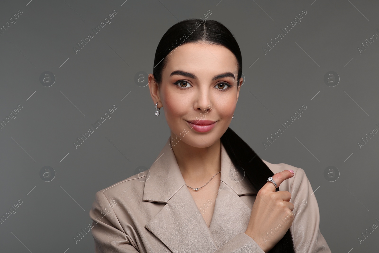 Photo of Beautiful young woman with elegant jewelry on dark grey background