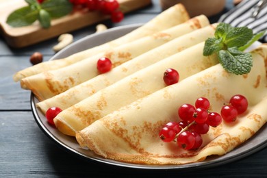 Photo of Delicious thin pancakes with berries on blue wooden table, closeup