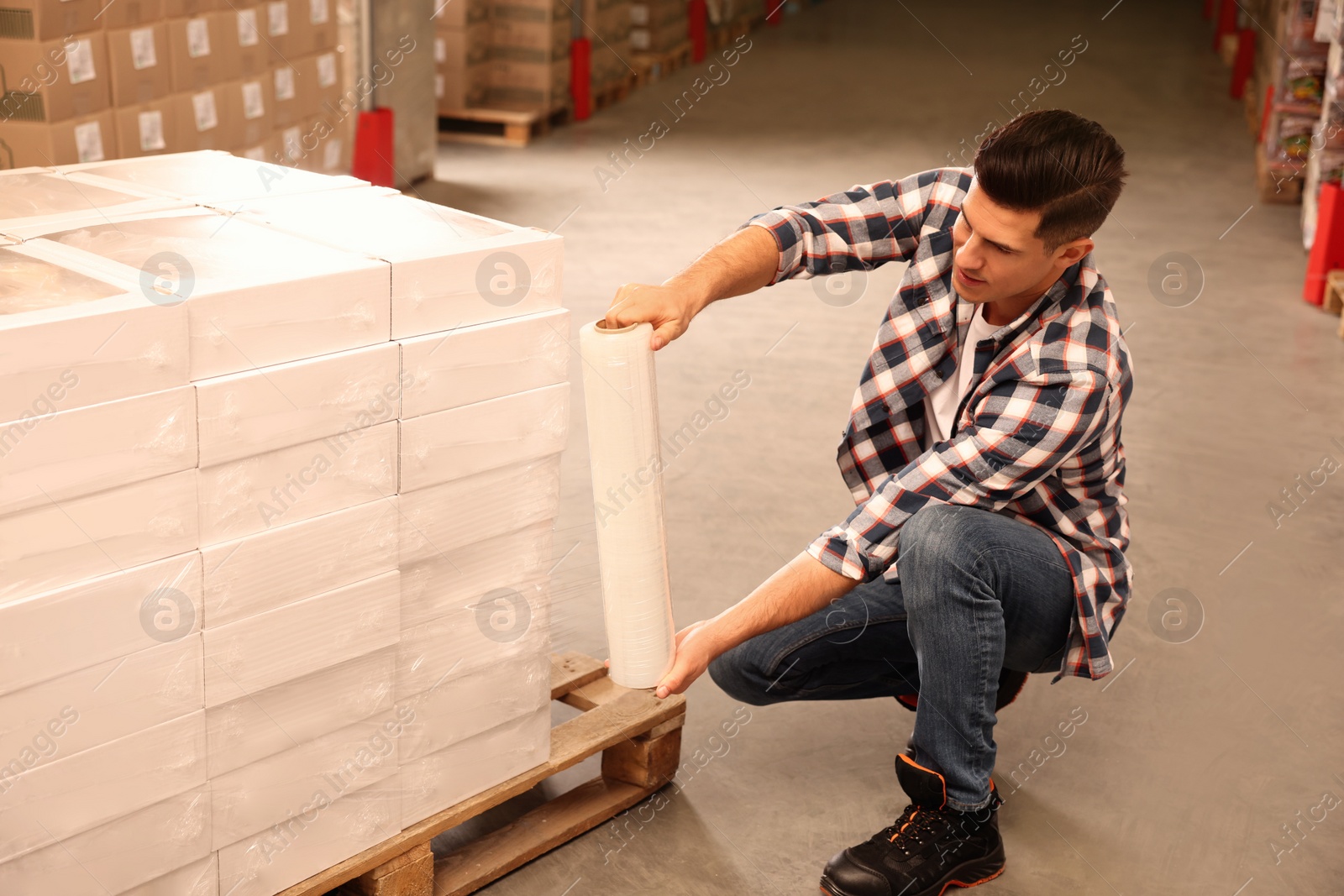 Photo of Worker wrapping boxes in stretch film at warehouse