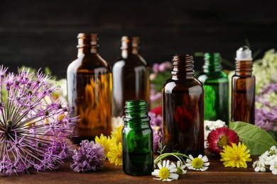 Photo of Different bottles of essential oils and flowers on table