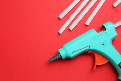 Photo of Turquoise glue gun and sticks on red background, flat lay. Space for text