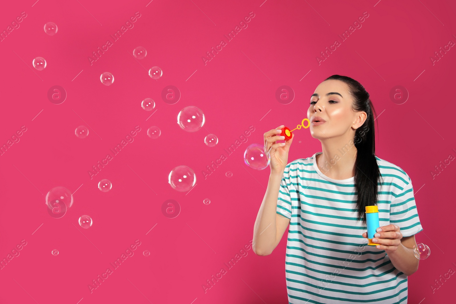 Photo of Young woman blowing soap bubbles on pink background, space for text