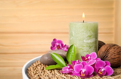 Photo of Composition with candle, spa stones and orchid flowers on table against wooden background