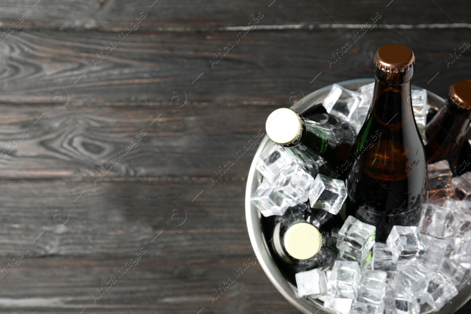 Photo of Metal bucket with bottles of beer and ice cubes on black wooden background, top view. Space for text