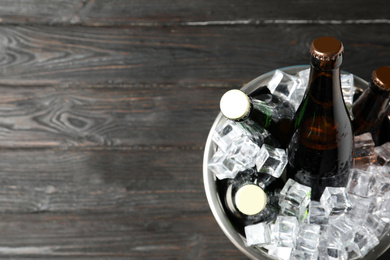 Metal bucket with bottles of beer and ice cubes on black wooden background, top view. Space for text