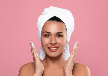 Beautiful woman applying facial cleansing foam on pink background