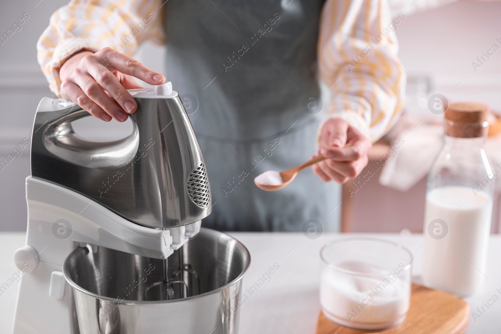 Photo of Woman adding sugar into bowl of stand mixer while making dough at table indoors, closeup