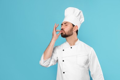 Photo of Mature chef showing delicious gesture on light blue background, space for text