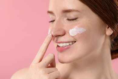 Smiling woman with freckles and cream on her face against pink background, closeup. Space for text