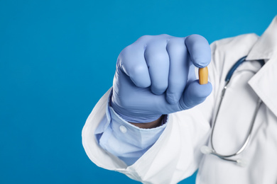 Photo of Doctor holding suppository for hemorrhoid treatment on blue background, closeup