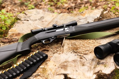 Hunting rifle, cartridges and binoculars on tree stump outdoors, closeup