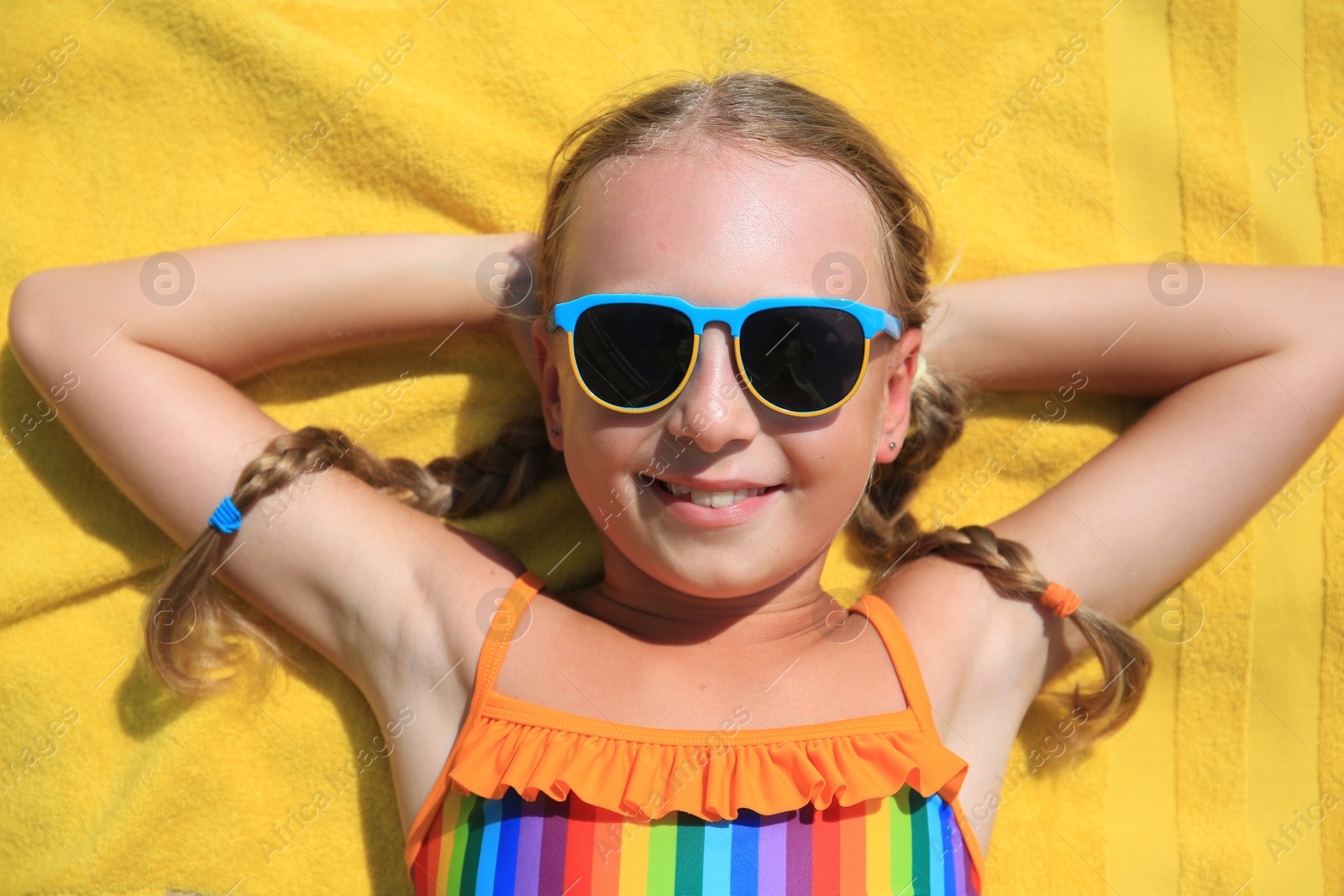 Photo of Happy little girl in sunglasses lying on beach towel outdoors, top view