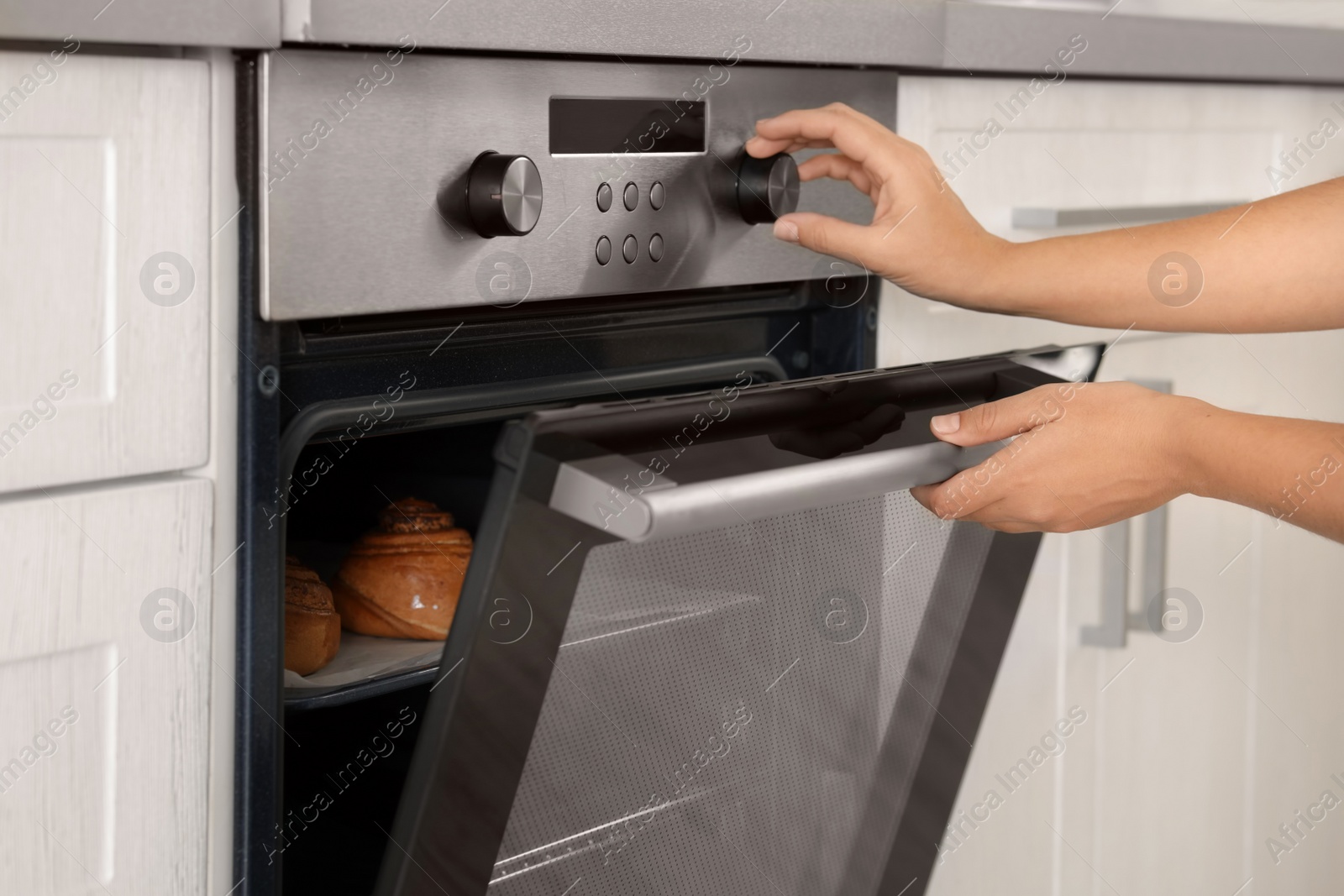 Photo of Young woman baking buns in electric oven, closeup