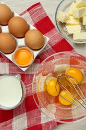 Photo of Whisk, eggs in bowl, milk and butter on white wooden table, flat lay